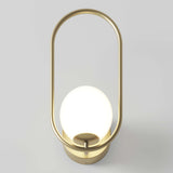 A modern wall sconce with a brass oval frame and a glowing white glass globe as the light source, mounted on a light-colored wall.
