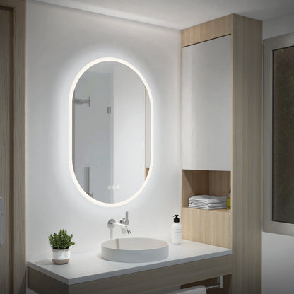 Modern bathroom with an Artika Clara 30x20 in. oval LED mirror, white sink, plant, soap dispenser, shelves, and a window.