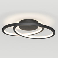 The Artika Salto LED flush mount light features two intersecting black circular LED rings emitting a soft white glow, mounted on a round base against a plain white ceiling.