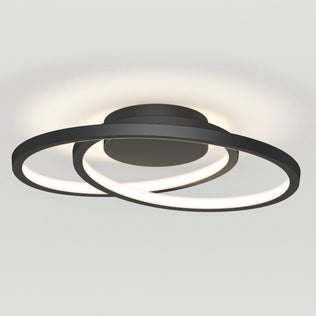 The Artika Salto LED flush mount light features two intersecting black circular LED rings emitting a soft white glow, mounted on a round base against a plain white ceiling.
