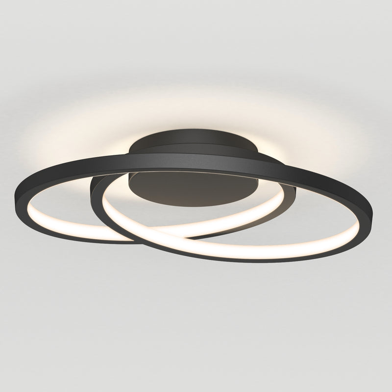 The Artika Salto LED flush mount light features two intersecting black circular LED rings emitting a soft white glow, mounted on a round base against a plain white ceiling.