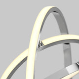Close-up of a modern light fixture with intersecting metallic rings and integrated LED strips emitting a soft, warm white glow, set against a plain gray background.