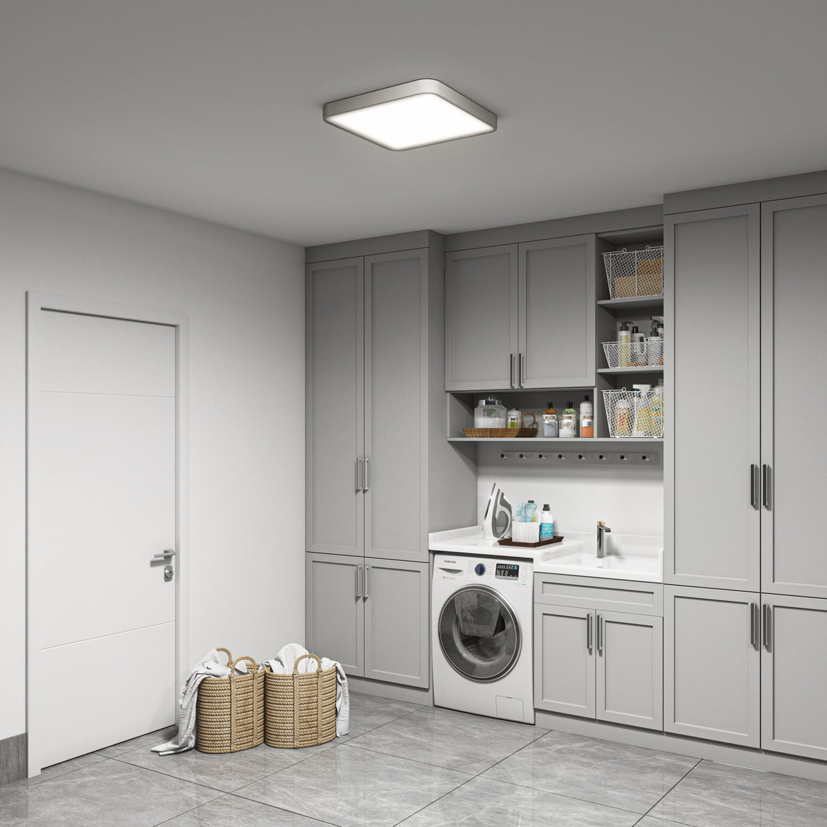 A modern laundry room features gray cabinets, a front-loading washer, sleek countertops with a sink, open shelves for cleaning supplies, wicker baskets holding towels on tiled floors, and is illuminated by the Artika Europa 18 in. LED flush mount light with remote.