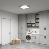 A modern laundry room with gray cabinets, a front-loading washing machine, a built-in sink, shelves with cleaning supplies, and two wicker laundry baskets filled with towels on a tiled floor.