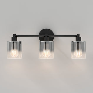 The Artika Haze modern 3-light bathroom vanity light features three exposed bulbs in clear cylindrical glass shades, shown mounted on a light gray wall.