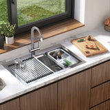 Modern kitchen sink with a high-arc faucet, over-sink dish rack, and organized compartments, set in a marble countertop. A wooden cutting board with vegetables and fruit sits nearby under a large window.