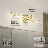 Modern gold-finished, integrated LED light fixture with a unique twisted design mounted above a bathroom mirror. Labels highlight its energy efficiency and 5-year warranty. Shelves and a shower are visible in the background.