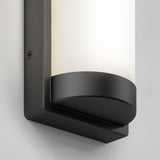 Close-up of a modern wall-mounted cylindrical light fixture with a matte black base and a frosted white cover, attached to a light gray wall.