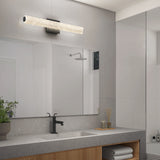 Modern bathroom with a large mirror, black faucet, rectangular sink, wooden vanity, and a long, horizontal light fixture above the mirror. Towels and toiletries are neatly arranged on shelves below the counter.