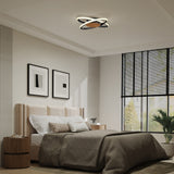 Modern bedroom with a beige upholstered bed, gray bedding, two abstract art prints, a round wooden nightstand, and a unique circular LED ceiling light. Large windows allow natural light into the room.