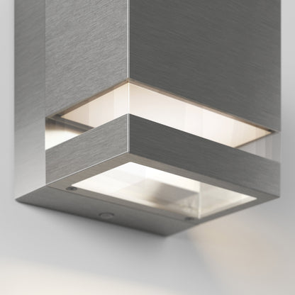 A close-up of the Artika-CAN-dev Valor Square LED indoor/outdoor wall light showcases its modern brushed metal design, emitting soft white light from the bottom and sides against a neutral background.