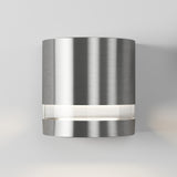 A modern cylindrical brushed metal wall sconce emits light from a narrow horizontal opening near its base, mounted on a plain light-colored wall.