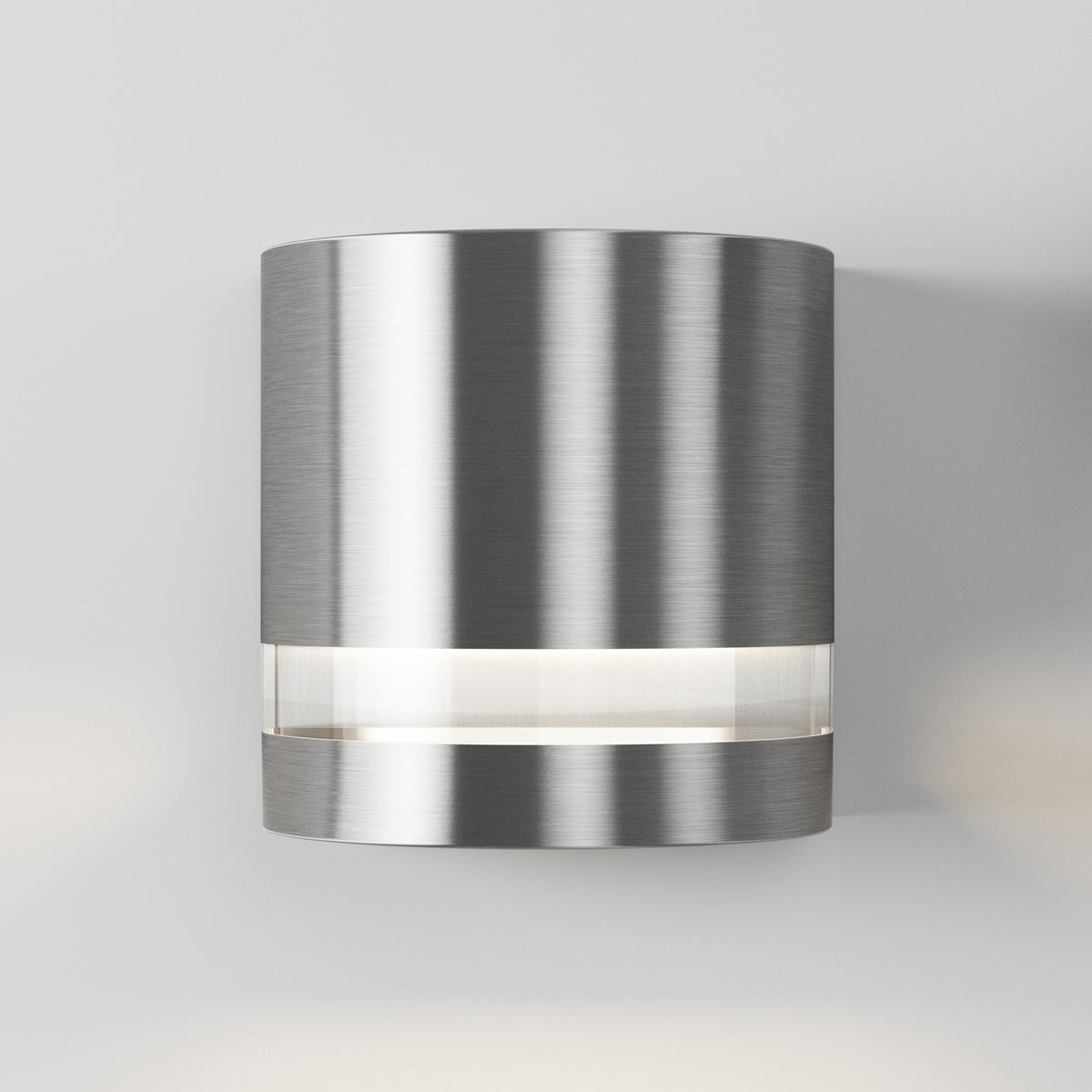 The Artika Valor Round LED indoor-outdoor wall light features a modern cylindrical brushed metal design with a horizontal frosted band emitting soft white light, shown mounted on a plain light gray wall.