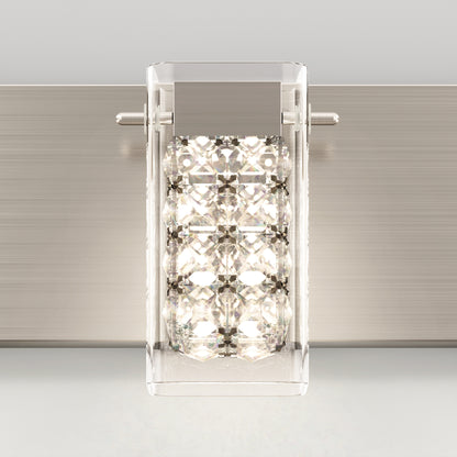A modern wall sconce with a rectangular metallic base and a clear glass shade, featuring a grid of sparkling crystal-like elements that reflect the light inside.