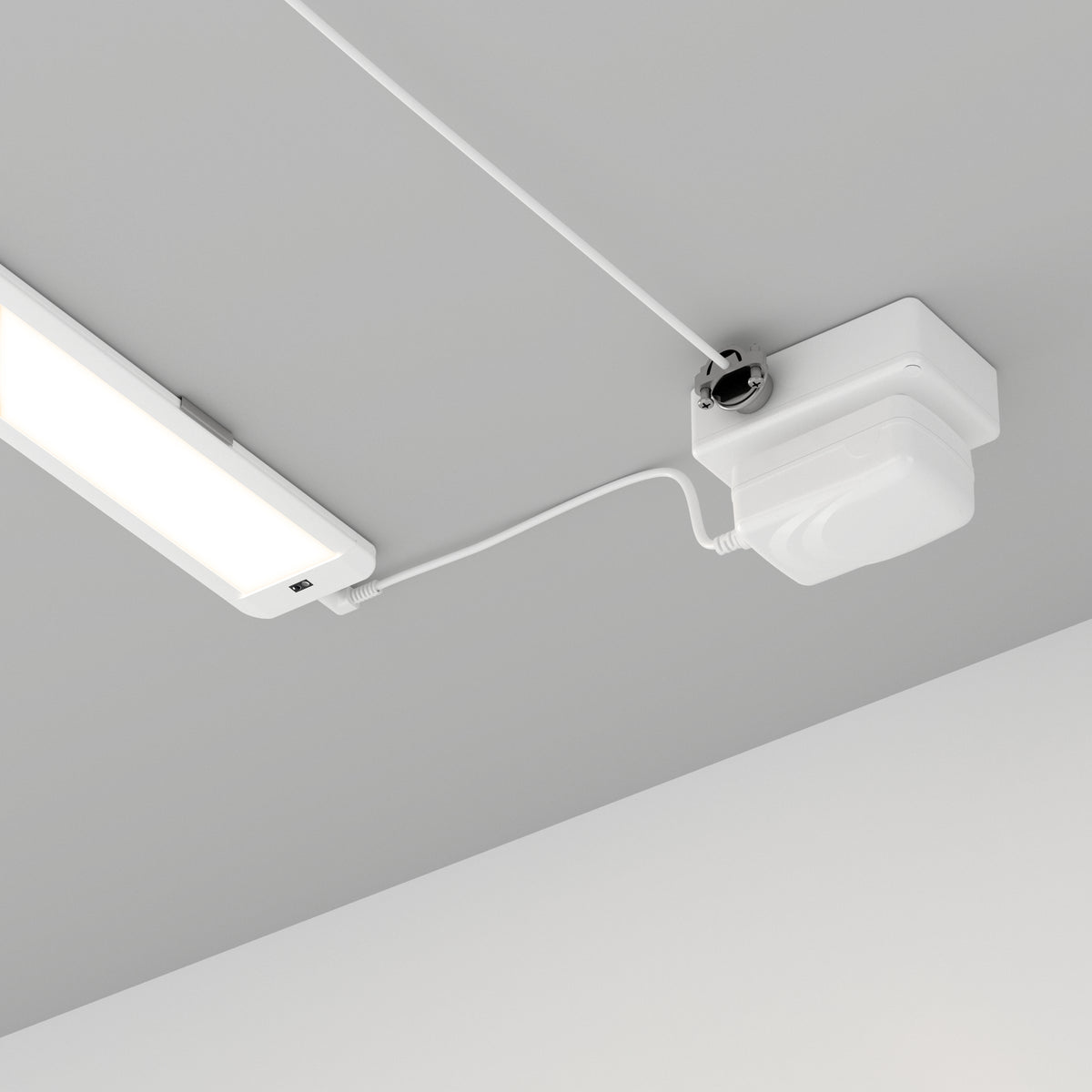 A white rectangular LED light fixture and a connected white electrical device are mounted on a gray ceiling, with visible wiring running between the two components.