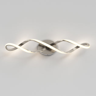 The Artika Swirl LED bathroom vanity light features two intertwined, wave-shaped arms on a round metallic base, emitting a soft white glow.