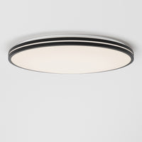 The Artika Athos 21 in. LED flush mount light, featuring a modern design with black and white layered edges, is installed on a plain white ceiling and emits a soft, diffused glow. Includes remote control for convenience.