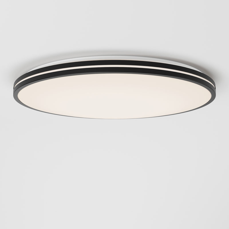 The Artika Athos 21 in. LED flush mount light, featuring a modern design with black and white layered edges, is installed on a plain white ceiling and emits a soft, diffused glow. Includes remote control for convenience.