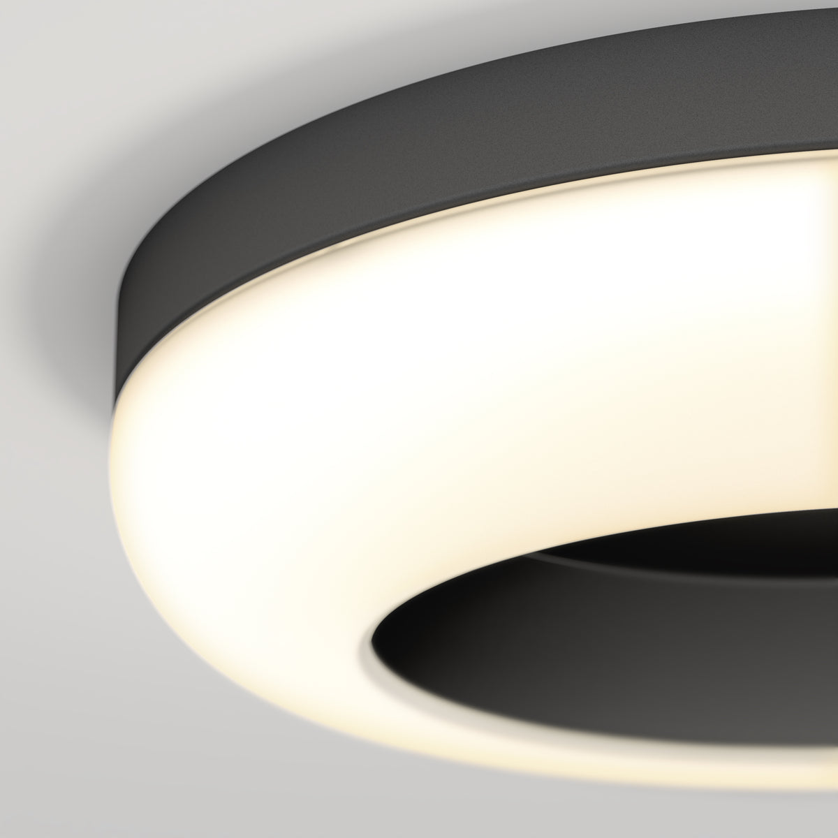 A close-up view of a modern, circular ceiling light fixture with a black outer rim and a glowing white light, mounted on a white ceiling.