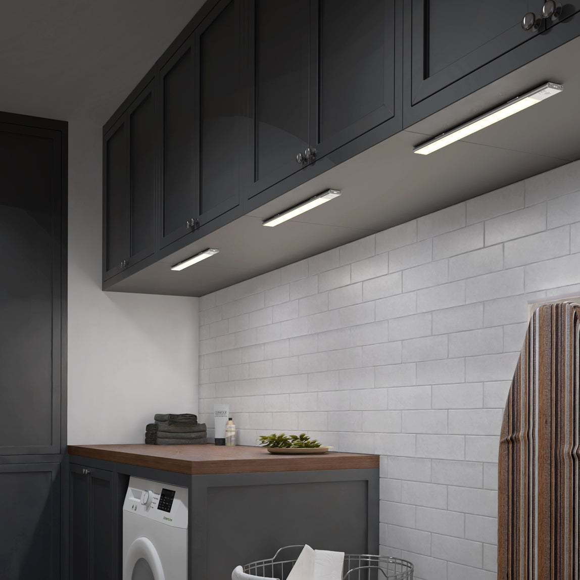 A laundry room with dark cabinets, white subway tile backsplash, under-cabinet lighting, a wooden countertop, a washing machine, folded towels, and an ironing board visible on the right.