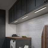 A laundry room with dark cabinets, white subway tile backsplash, under-cabinet lighting, a wooden countertop, a washing machine, folded towels, and an ironing board visible on the right.