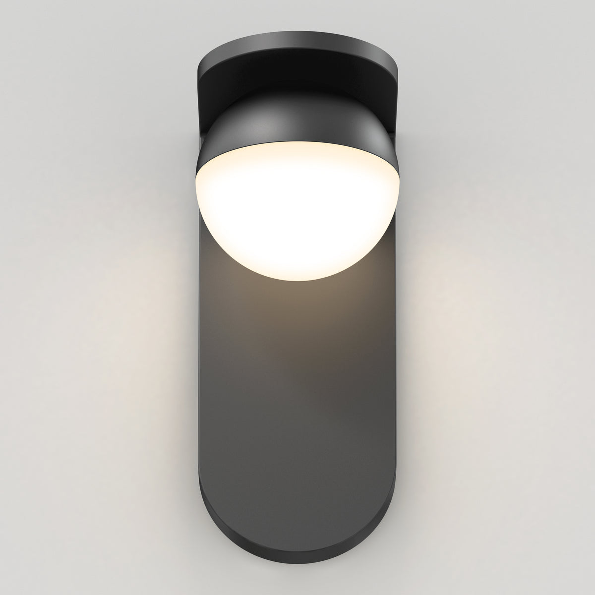 A modern black wall sconce with a rounded base and a dome-shaped, glowing white light fixture mounted on a plain, light-colored wall.