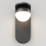 A modern black wall sconce with a rounded base and a dome-shaped, glowing white light fixture mounted on a plain, light-colored wall.