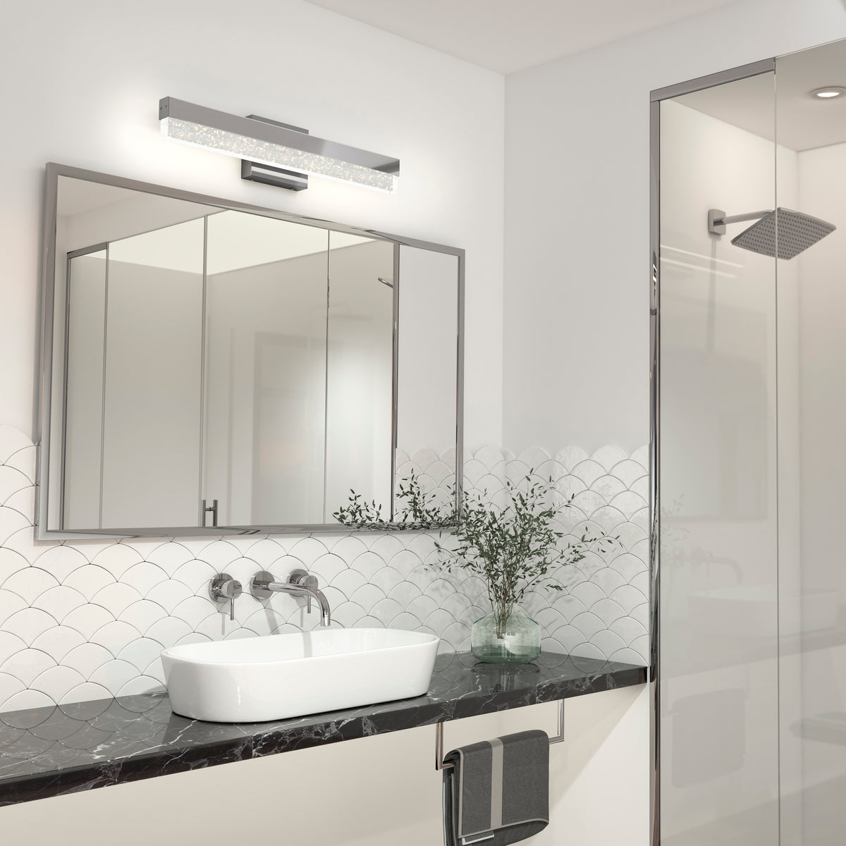 Modern bathroom with a white vessel sink on a black marble countertop, a large mirror above with a sleek light fixture, a glass shower, a towel hanging, and a small plant for decoration.