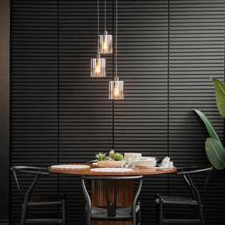 A modern dining area featuring a round wooden table for four, black chairs, a Haze modern 3-light glass pendant by Artika above, a textured black wall, and a large green plant on the right.