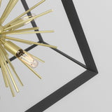 Close-up of a modern chandelier with gold, spiky rods and exposed filament bulbs, framed by a black square structure against a plain, light background.