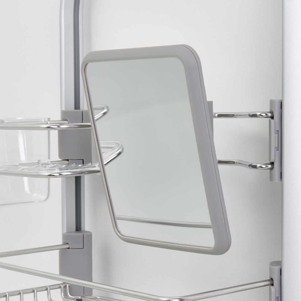 A close-up of a rectangular mirror with a grey frame mounted on a metal bathroom shelf unit. The mirror is attached with metal brackets and slightly angled to the side.