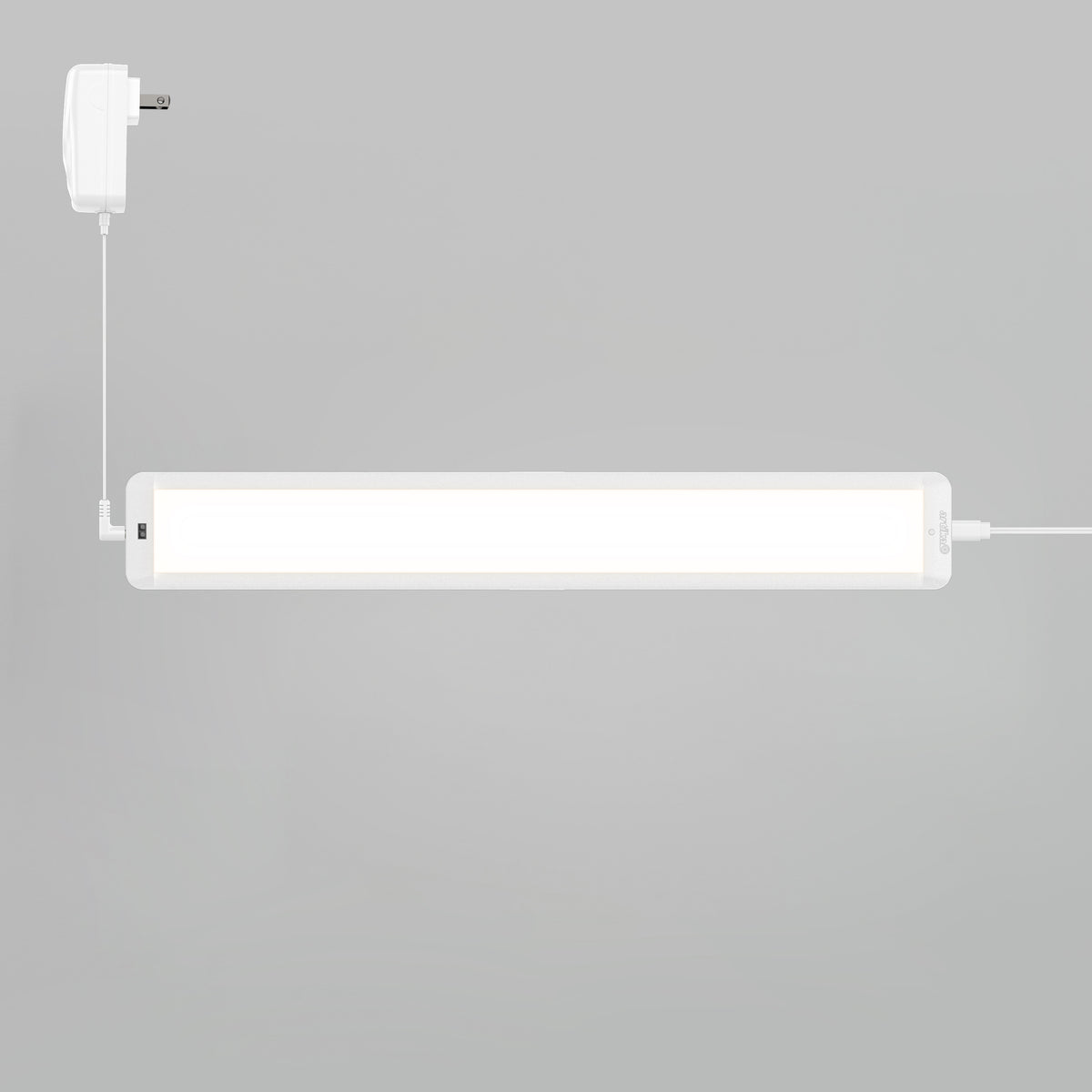 The Artika Maestro under cabinet LED light 3CCT is installed on a light grey wall, with a white power adapter connected by a cable on the left.