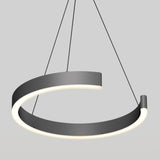A modern, circular black pendant light hangs from the ceiling by three thin wires. The light fixture has an open ring design with built-in LED illumination along the inner edge, set against a plain gray background.