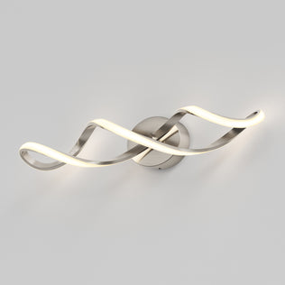 The Artika Swirl LED bathroom vanity light features two intertwined, wave-like LED strips mounted on a round metallic base, softly illuminating a plain light gray wall.