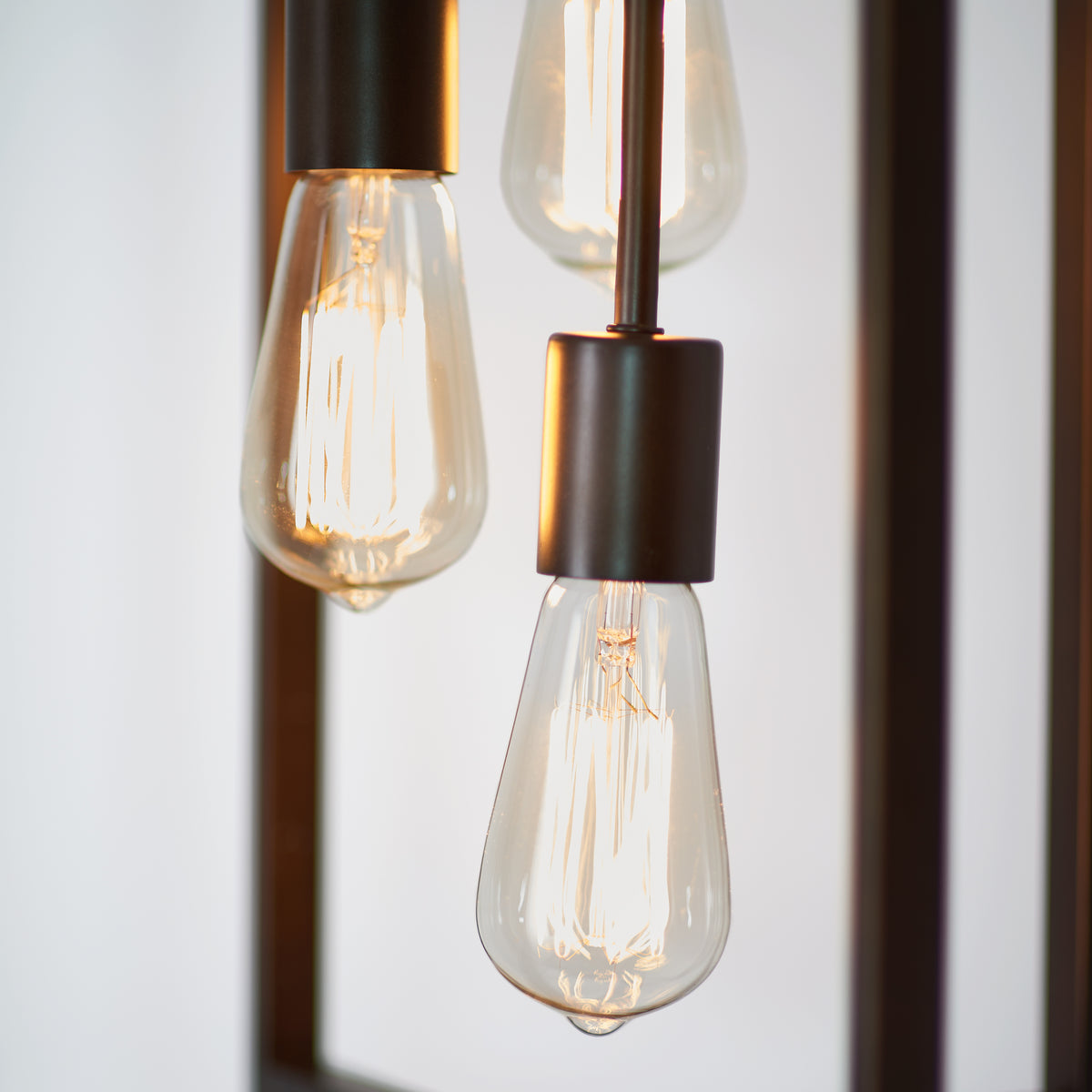 Close-up of three illuminated vintage-style Edison light bulbs with exposed filaments, hanging from metallic sockets against a softly blurred background.