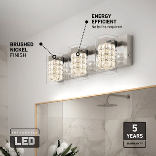 Artika’s Crystal Cube LED bathroom vanity light 5 CCT features three crystal-inspired lights in a brushed nickel finish above a mirror. Integrated LED delivers energy efficiency and comes with a 5-year warranty. White flowers are also in view.