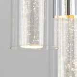 Close-up of a modern glass pendant light with bubbles inside the cylindrical glass shade, illuminated and hanging against a plain, light gray background.