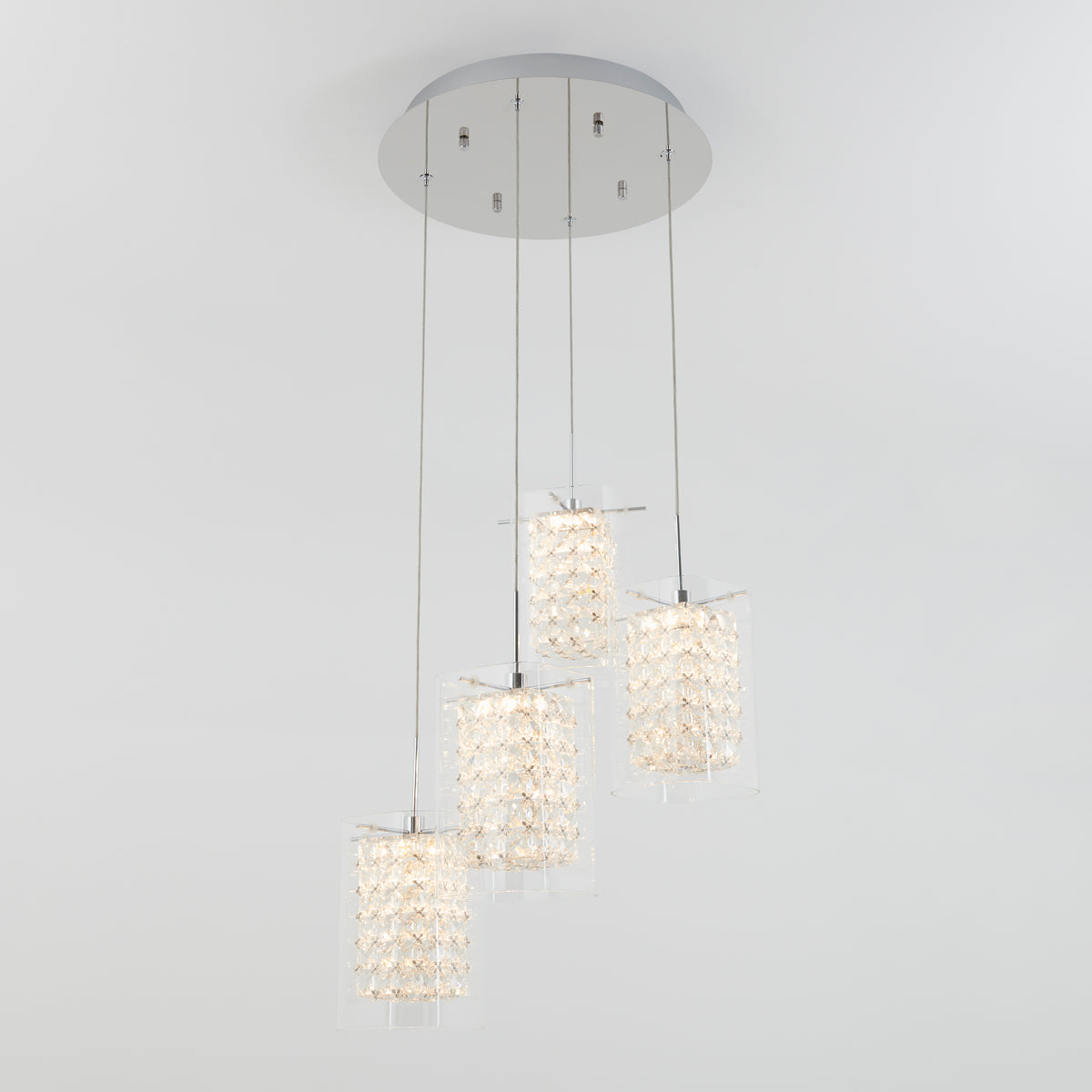A modern ceiling light fixture with a round base and four hanging pendant lights, each featuring a cylindrical crystal design, is suspended at varying heights against a plain white background.