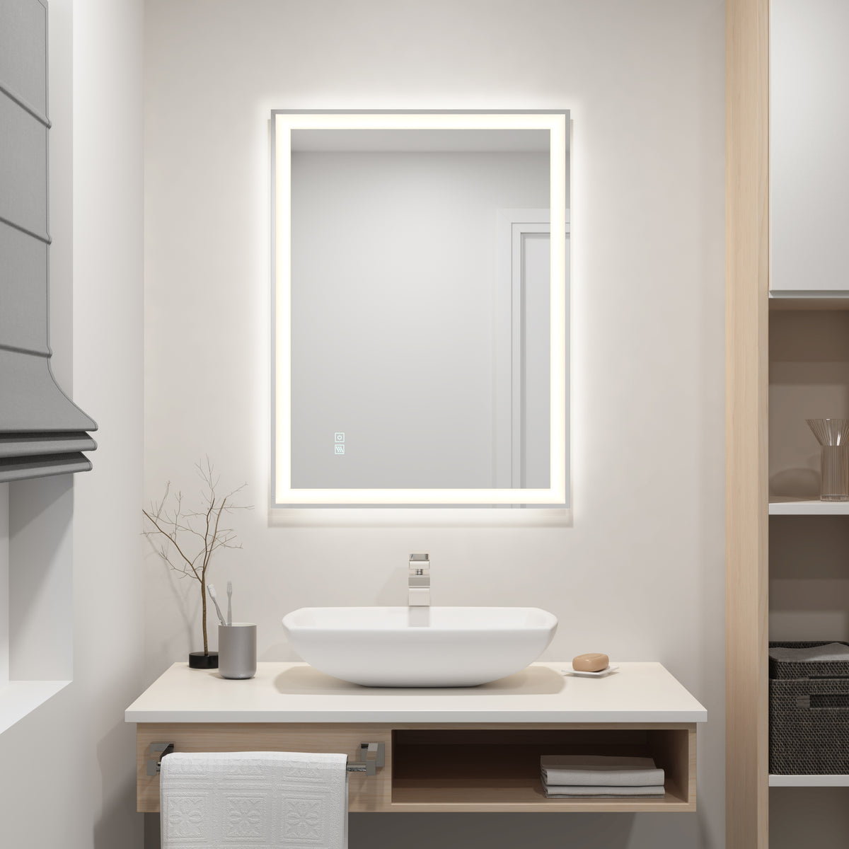 A modern bathroom with a rectangular, backlit mirror above a white sink on a floating vanity. Minimalist decor includes a small plant, soap dispenser, cup, and folded towel. Open shelves hold towels and glassware.
