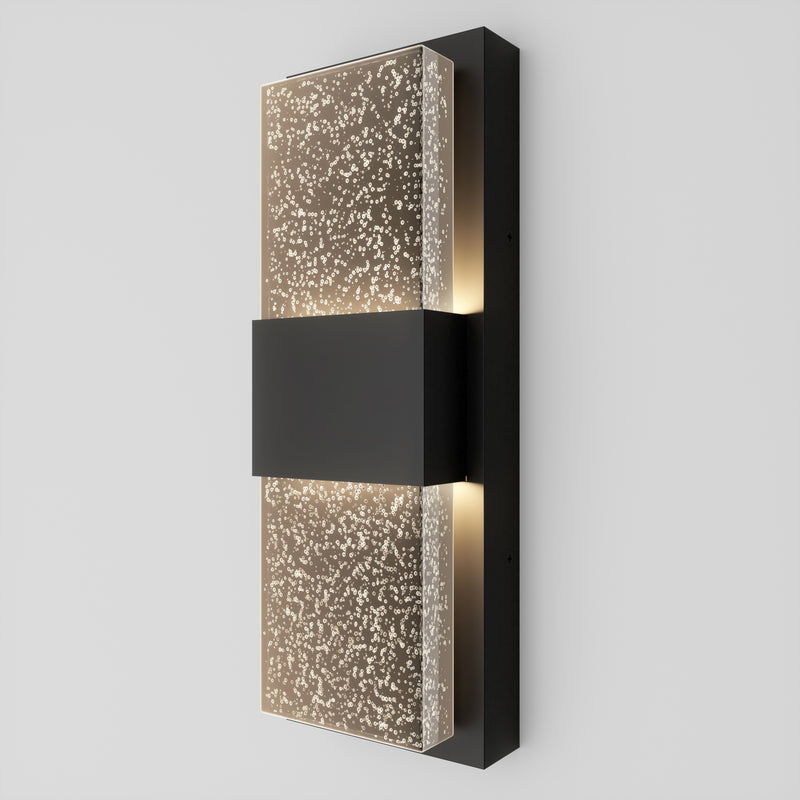 The Artika Mazza Bubble indoor-outdoor LED wall light features a modern design with a rectangular black center and frosted glass panels adorned with a dotted pattern, providing soft illumination on any light-colored wall.