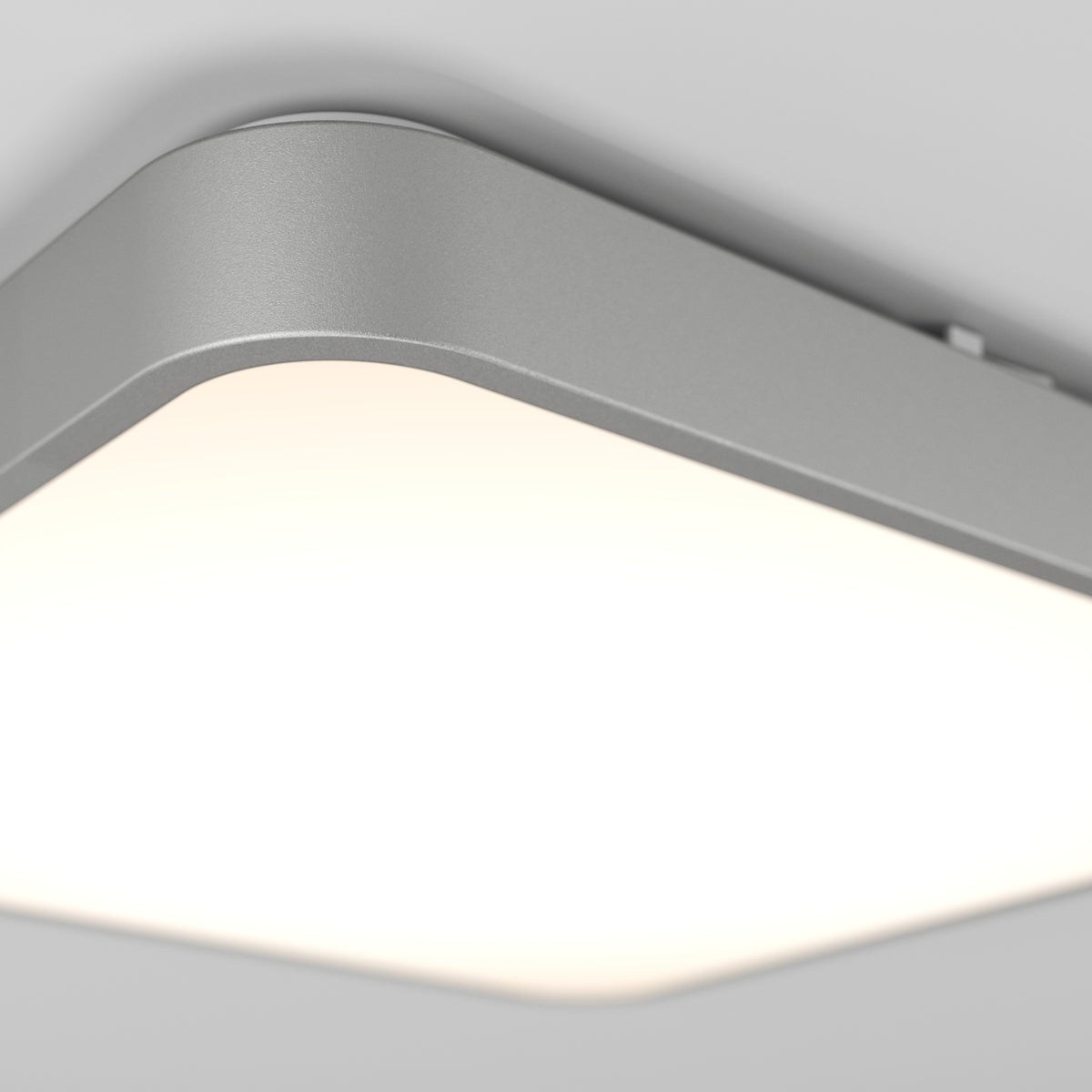 Close-up view of a modern, rectangular ceiling light fixture with a smooth, metallic frame and a bright, even white light diffused through its surface, mounted on a light-colored ceiling.