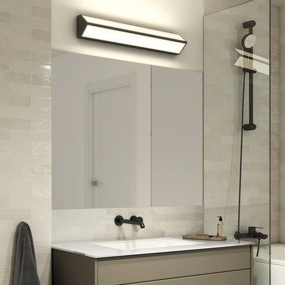 A modern bathroom featuring Artikas Preston LED vanity light, light beige subway tiles, a rectangular mirror, black wall-mounted faucet, white sink, towel on the wall, and a glass shower with black showerhead.