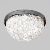 A close-up of a modern crystal ceiling light fixture with a round, faceted glass shade and a glossy metallic rim, mounted against a plain light gray background.