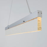 A modern rectangular pendant light with a frosted, glittery acrylic shade and a silver metal frame, suspended by two cables against a plain light gray background.
