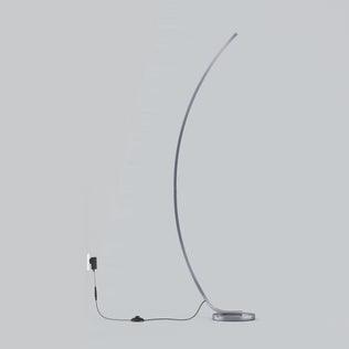 The Artika Arc LED Floor Lamp features a minimalist, modern arched design with a slim curve and round base. This dimmable floor lamp includes a visible black cord and switch, plugged into a wall outlet against a light gray background.