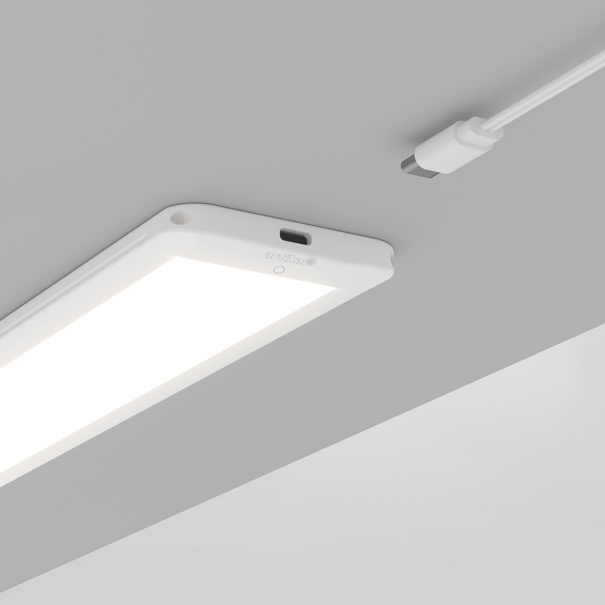 A rectangular LED ceiling light glows brightly on a gray ceiling. Above it, a white USB-C cable with a connector is positioned, appearing ready to plug into the light.