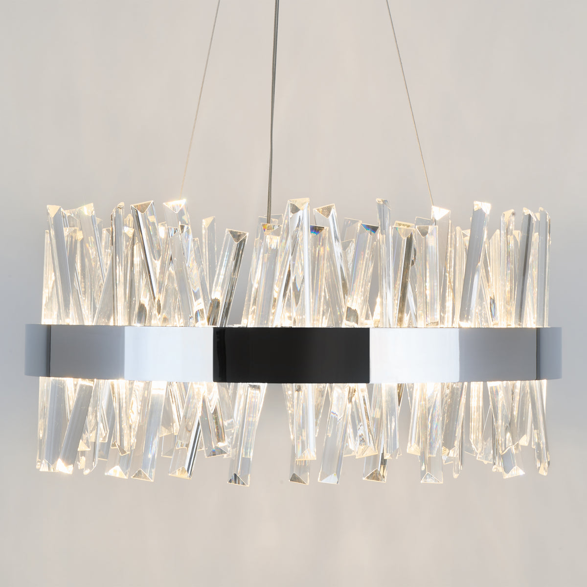 A modern chandelier with a circular metallic frame, featuring numerous crystal-like, angular glass pieces that reflect and refract the light, suspended from the ceiling by thin cables.