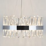 A modern chandelier with a circular metallic frame, featuring numerous crystal-like, angular glass pieces that reflect and refract the light, suspended from the ceiling by thin cables.