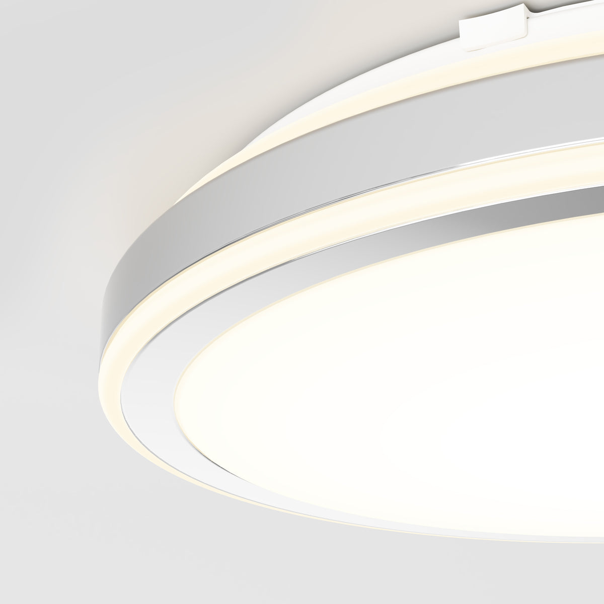 A close-up view of a modern, circular ceiling light fixture with a sleek, white and silver design, glowing brightly against a white ceiling.