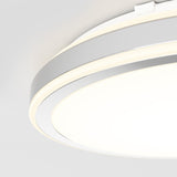 A close-up view of a modern, circular ceiling light fixture with a sleek, white and silver design, glowing brightly against a white ceiling.